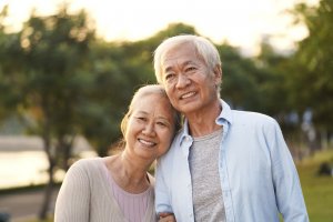 Older couple smiling and holding each other as they're on a walk surrounded by trees and nature.