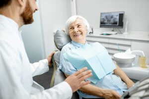 Happy older woman sitting in a dentist chair speaking to the dentist.