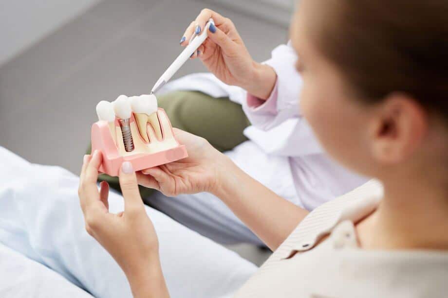 Patient in dental chair holding dental implant and crown model 920x613